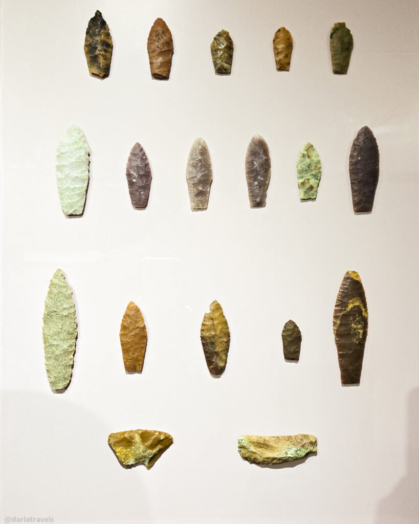Collection of ancient projectile points made of various stones, displayed on a white background.