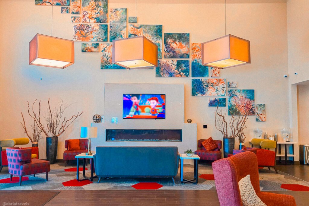 Hotel lobby in Loveland, Colorado, with colorful seating, three square pendant lights, and a large multi-panel abstract artwork above a fireplace.