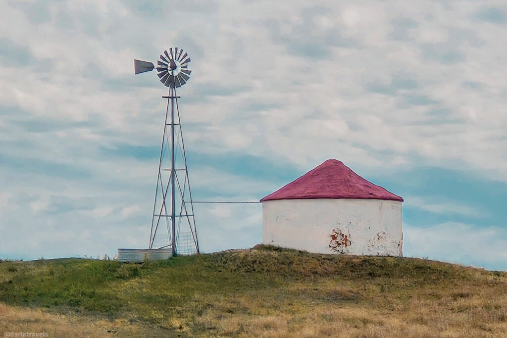 Windmill beside a round white water storage tank with a red roof on the plains near Julesburg.