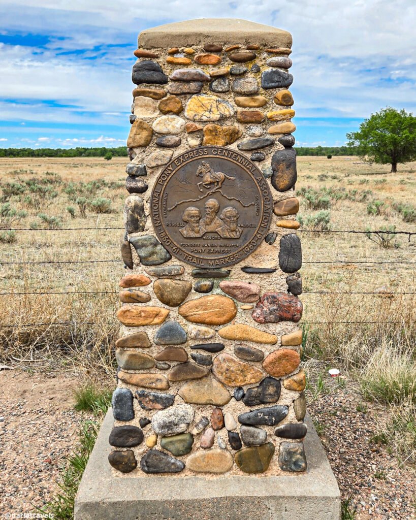 Pony Express centennial trail marker with portraits of Russell, Majors, and Waddell on a stone pillar.