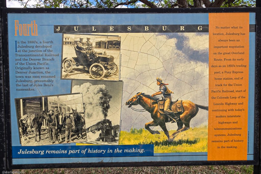'Fourth Julesburg' interpretive panel with historic photographs of a car, horses, and a steam locomotive.