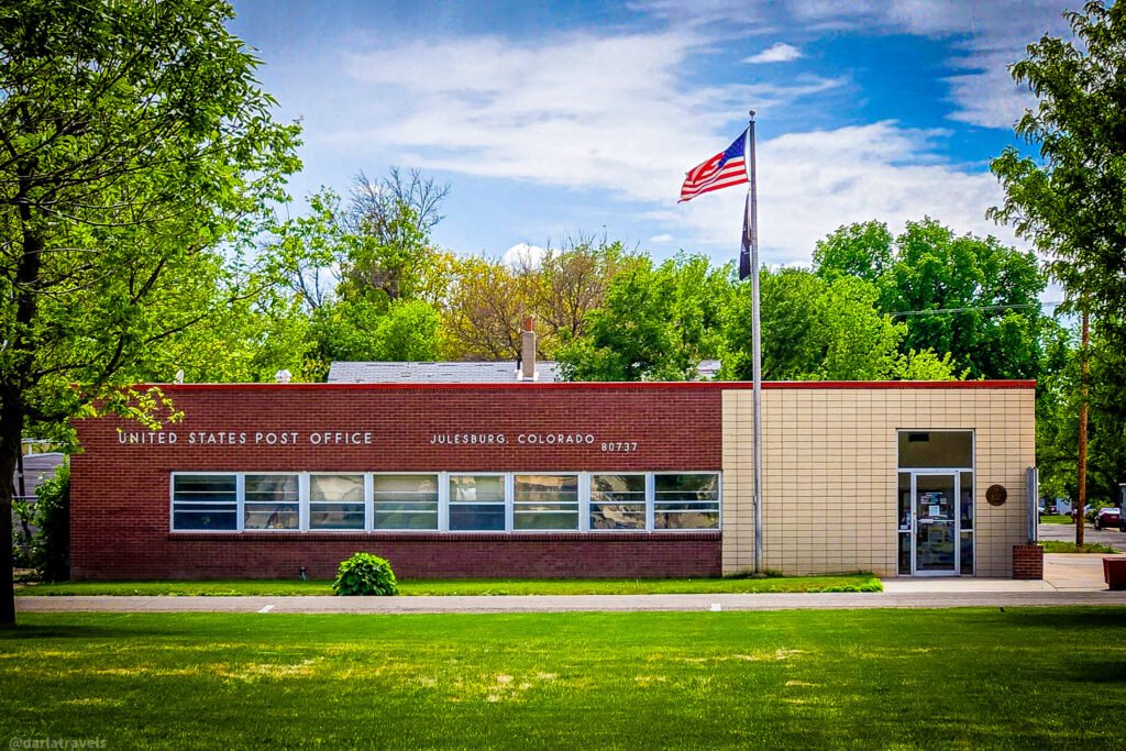 Julesburg post office exterior with red brick, a light-colored entrance section, and an American flag.
