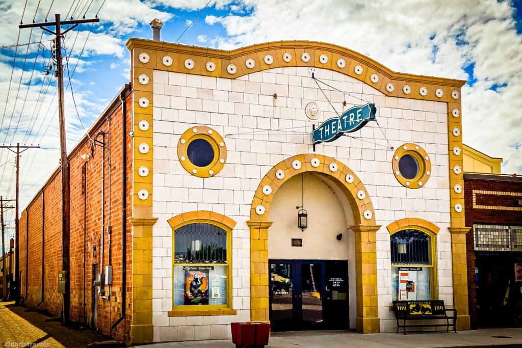 Julesburg Hippodrome Arts Center theater facade with white-and-gold trim, round windows, and a recessed arched entrance.
