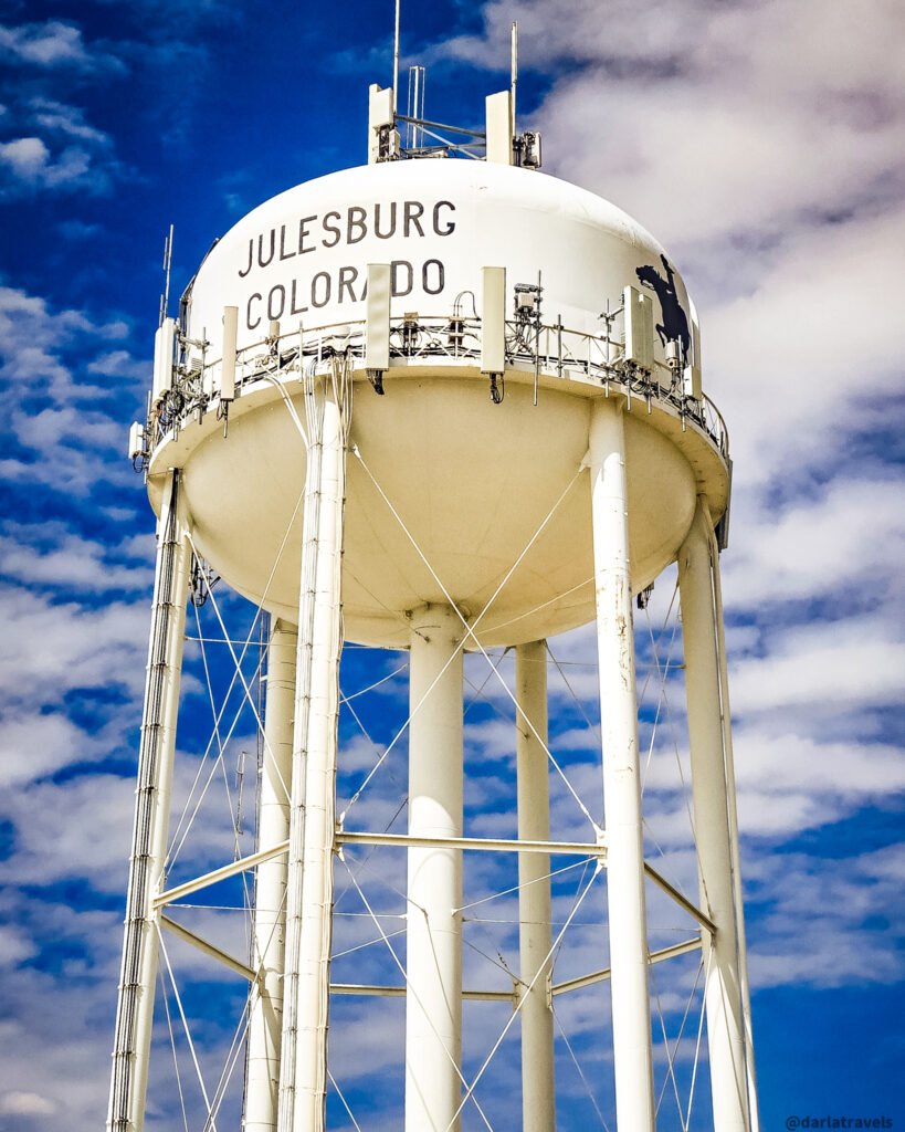 White Julesburg water tower with town lettering, a mounted-rider silhouette, and communications antennas.