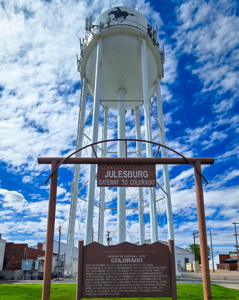 Julesburg water tower above a 'Gateway to Colorado' sign and a historical marker.