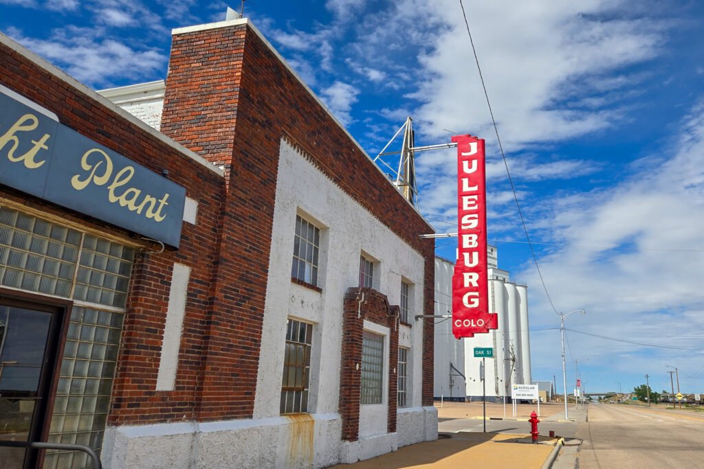 Julesburg Power Plant building with a vertical red 'Julesburg Colo' sign above the sidewalk.