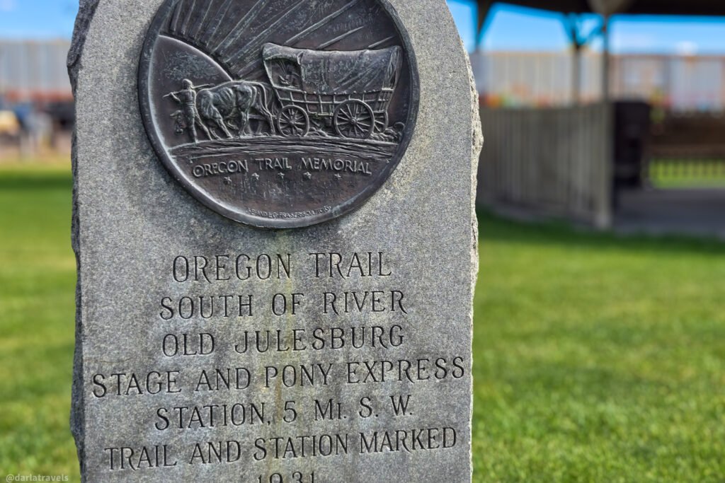 Oregon Trail memorial with a covered-wagon relief and an inscription pointing to Old Julesburg southwest of town.