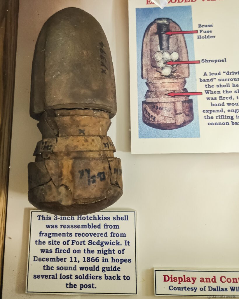 Reassembled 3-inch Hotchkiss shell beside a cutaway diagram and an exhibit label describing its recovery from Fort Sedgwick.