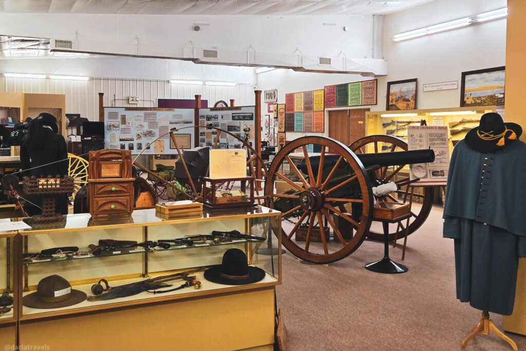 Fort Sedgwick Museum exhibits with a cannon, military clothing, and firearms in glass cases.