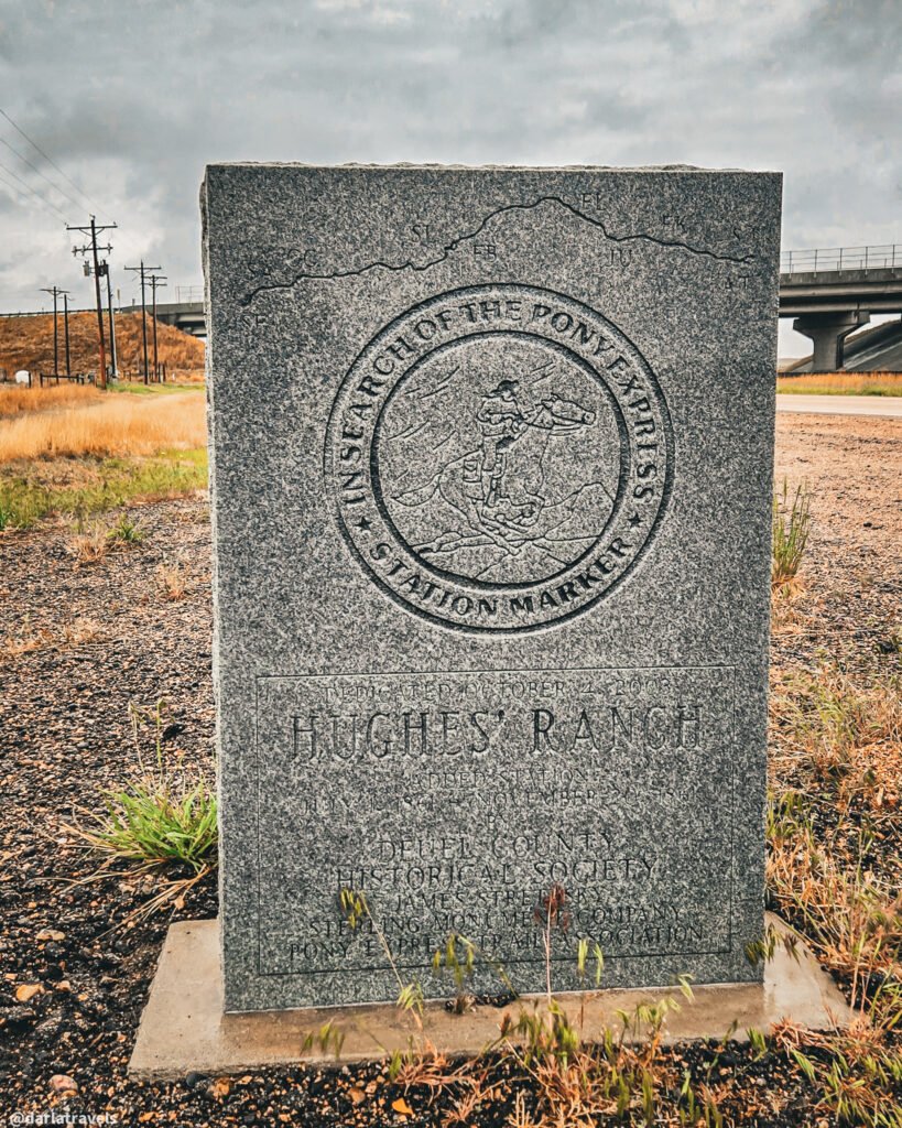 Hughes’ Ranch Pony Express marker with an engraved rider beside a highway overpass.