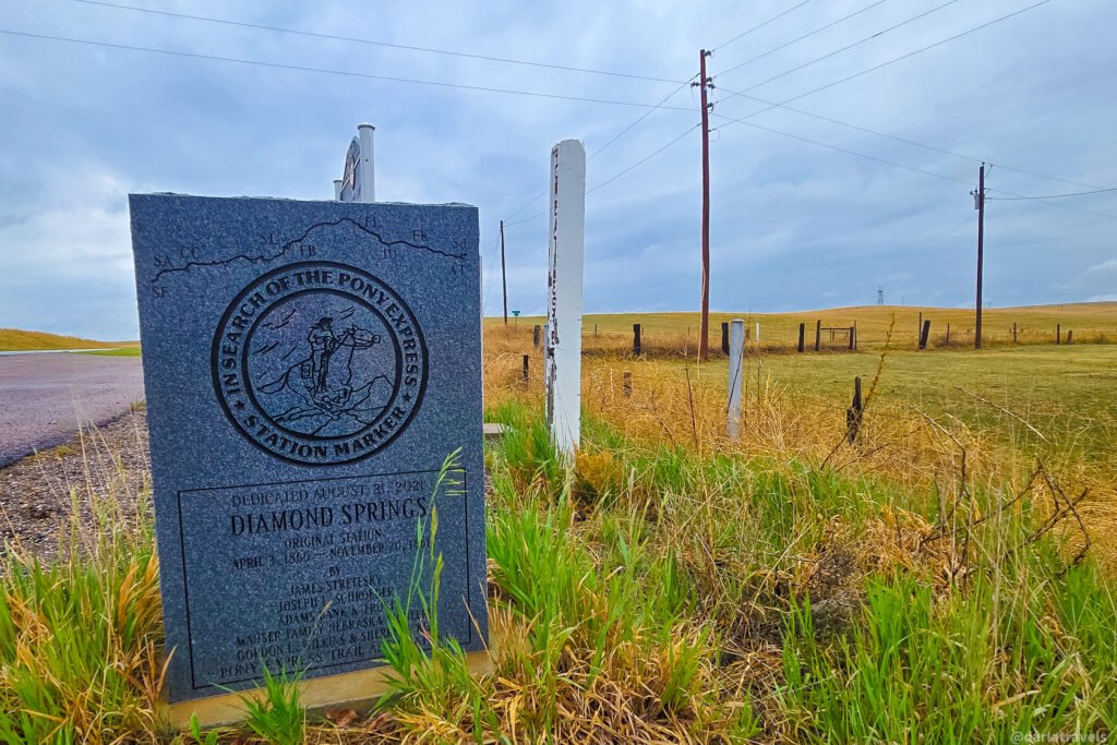 Diamond Springs Original Station marker with an engraved Pony Express rider beside fenced grassland.