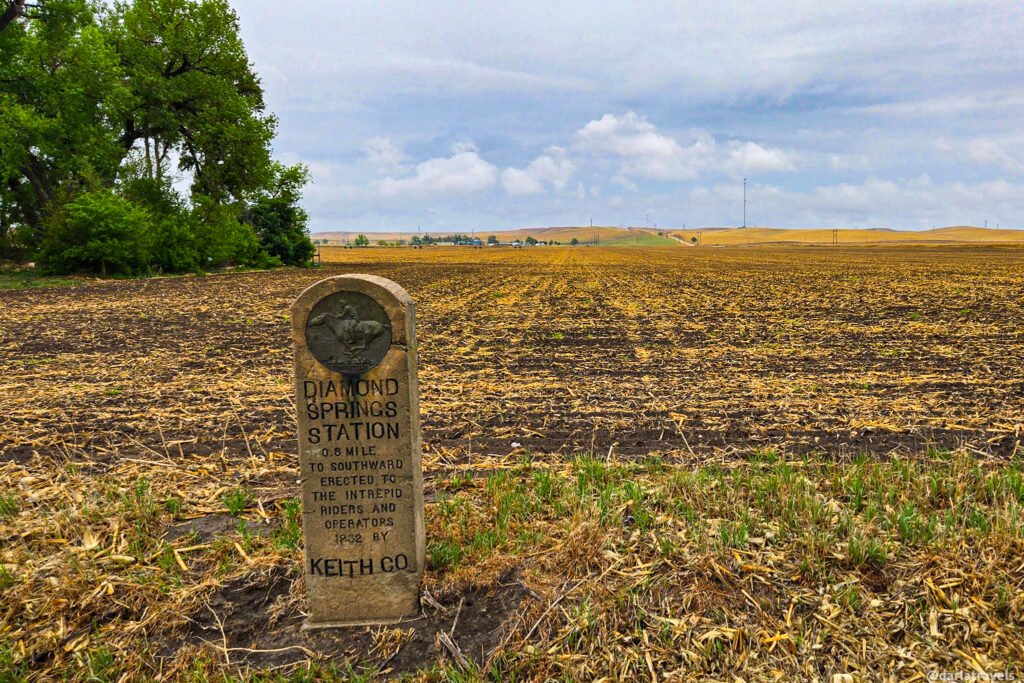 Diamond Springs Station stone marker with a Pony Express medallion at the edge of a cultivated field.