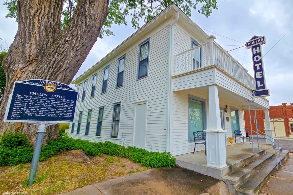 Phelps Hotel in Big Springs, with white siding, an upper balcony, a vertical hotel sign, and a historical marker.