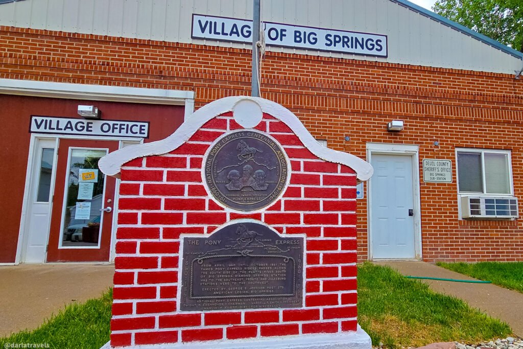 Red-brick Pony Express monument with bronze plaques outside the Village of Big Springs offices.