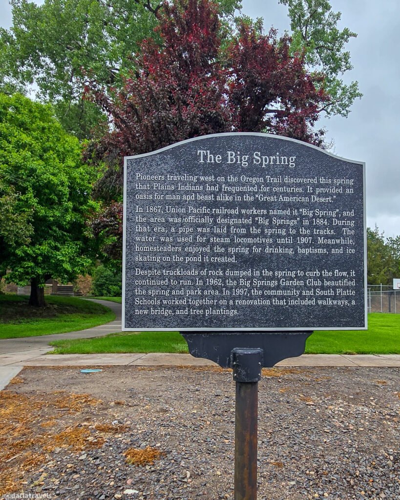 The Big Spring interpretive sign beside a tree-lined path in Big Springs, Nebraska.