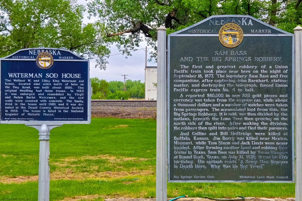 Waterman Sod House and Sam Bass train robbery historical markers standing side by side in Big Springs.